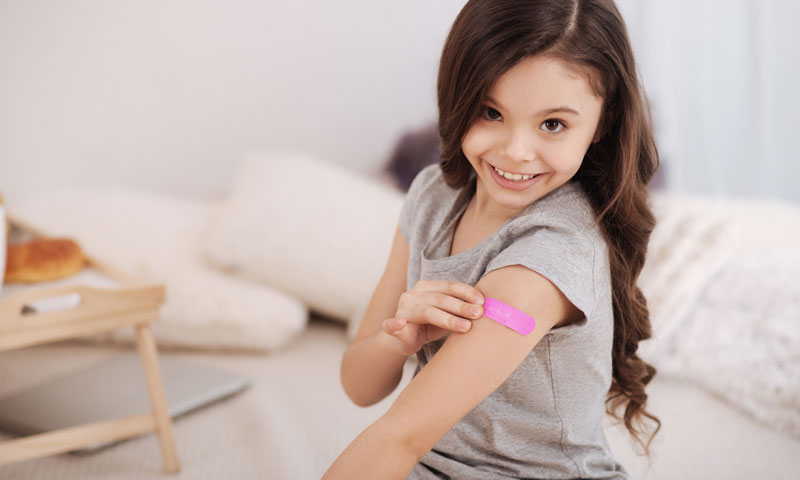 Little girl smiling with a pink band aid.